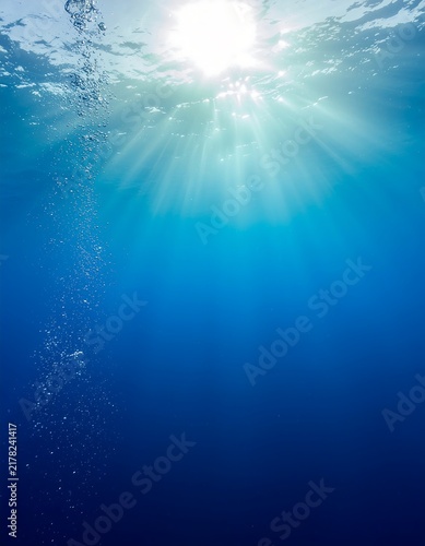 Underwater view of sunlight rays shining through deep blue ocean with rising air bubbles