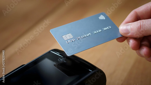 Contactless Payment: A person's hand holds a credit card near a payment terminal for a quick and easy transaction, highlighting modern commerce and technology.
