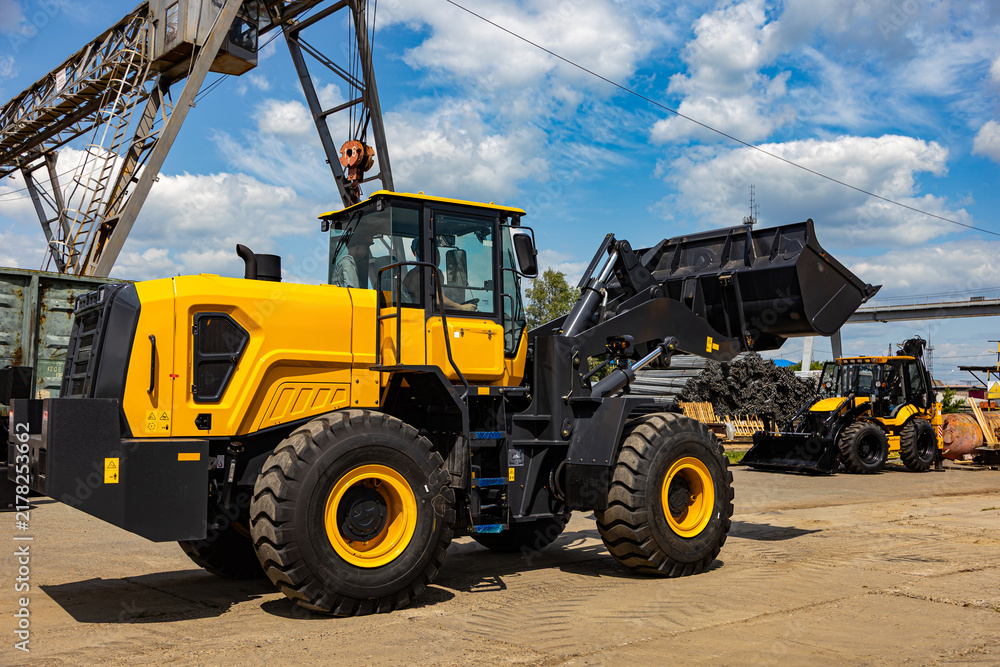 Fototapeta premium Large Yellow Wheel Loader with Raised Bucket at Industrial Yard