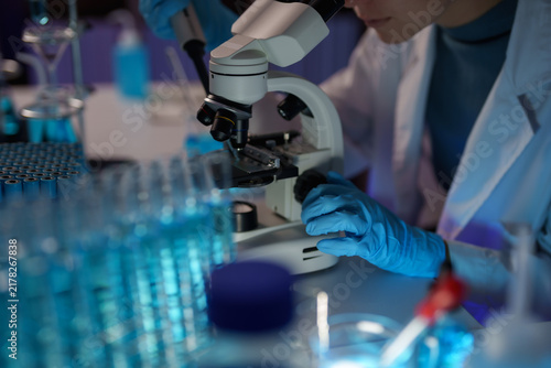 Fotografía Scientist in lab coat and blue gloves performing medical research using a micros