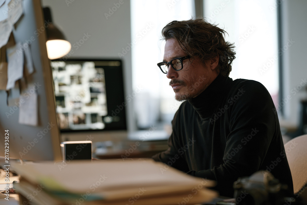 Obraz premium A stylish man analyzes creative work in a contemporary office filled with notes and designs, showcasing commitment and passion for the artistic process.