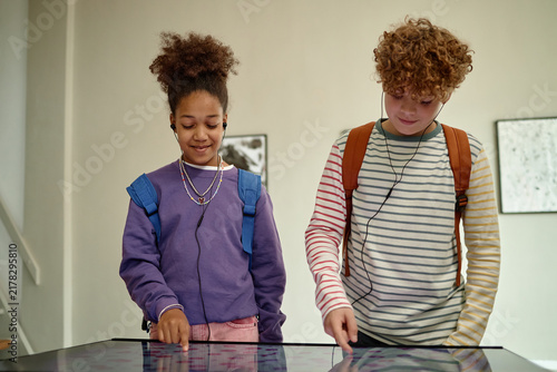 Diverse children, African American girl and Caucasian boy, using interactive digital screen in art gallery. Image represents modern museum education and interactive learning