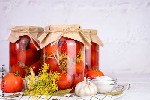 Homemade preserved tomatoes in glass jars with dill, garlic, bay leaves and spices. Seasonal food preservation. Close-up. Copy space.
