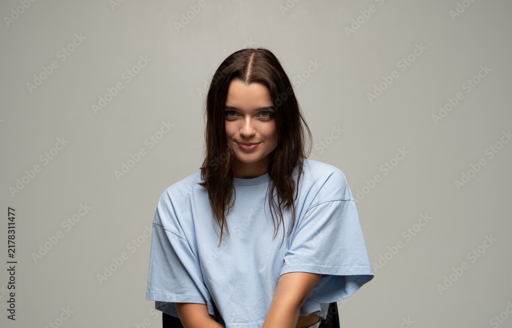 Naklejka premium Brunette young woman sitting, looking at camera, having engaging expression and posing in a studio portrait