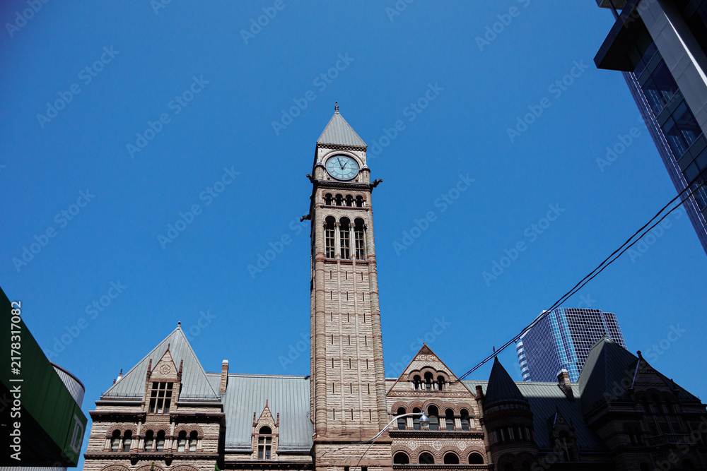 Obraz premium Historic Old City Hall clock tower framed by modern skyscrapers in downtown Toronto on a bright clear day. g.