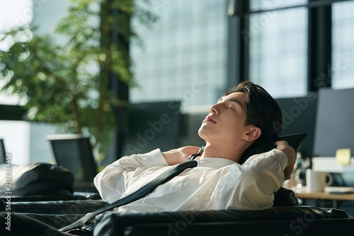 Young office worker relaxing in his chair with hands behind his head during a work break