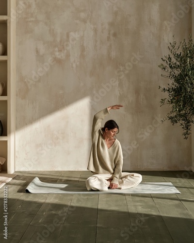 Woman stretching on a yoga mat in a quiet living room with muted tones and soft daylight, perfect for mindfulness and home wellness campaigns