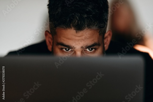 Focused man looking intently over top of his laptop screen during intense indoor work