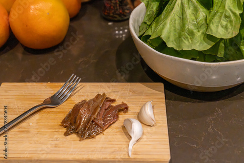 Anchovy fillets with garlic cloves on wooden cutting board for Mediterranean salad prep