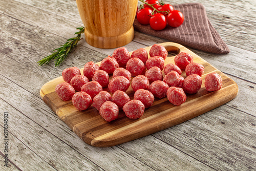 Quadro su tela Raw meatballs on wooden cutting board with fresh tomatoes and rosemary