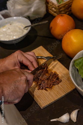 Chef hands slicing roasted meat for Mediterranean cuisine recipe on wooden board