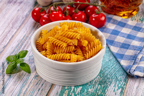 Foto Uncooked fusilli pasta in bowl with fresh cherry tomatoes and basil on rustic wo