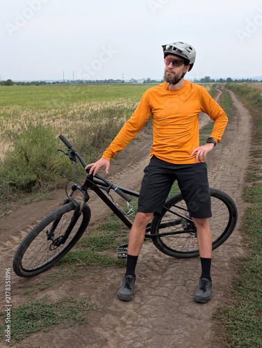 Cyclist on dirt road in orange shirt with mountain bike