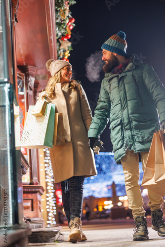 Couple walking down city streets, looking at display windows of stores while doing Christmas shopping
