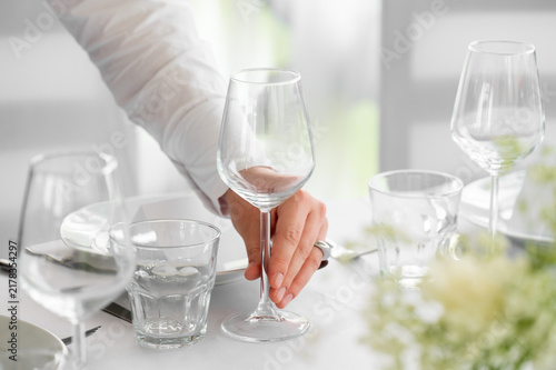 Waiter placing an elegant wine glass on a beautifully set white restaurant dining table