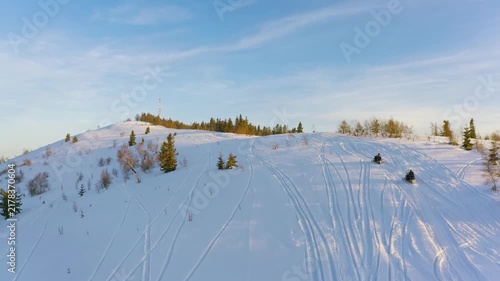 A man sitting on a snowmobile quickly rides along a snow-covered path among small spruce plants to a honeycomb tower against the backdrop of a fairy-tale sky