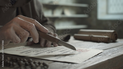 Bild auf Leinwand Hands of a monk guiding a small knife along text lines on parchment during readi