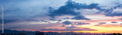 Cuadro en lienzo A serene twilight scene showing colorful sunset sky, scattered clouds, distant mountain ranges, and faint urban silhouettes on the horizon