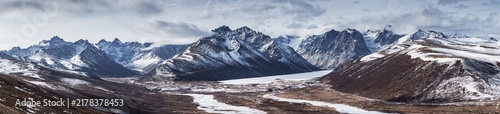 Фотография A panoramic view of a rugged snow-capped mountain range with frozen valleys under an overcast sky
