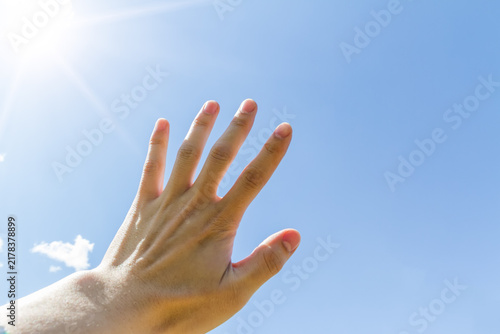 Konstfotografi A human hand reaches out towards the bright sun against a clear blue sky on a sunny day