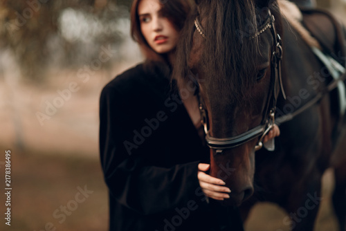 Canvastavla Young woman in black with her horse at sunset outdoors.