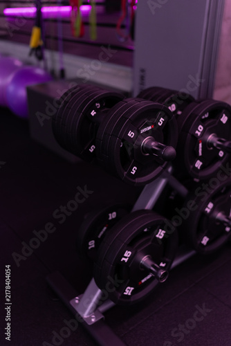 Fotografie Rows of black dumbbells on a modern gym rack with atmospheric purple lighting, creating a dramatic fitness and strength training scene