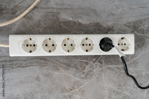 White power strip featuring six recessed, round sockets. Black power plug is shown inserted into the fifth socket from the left.