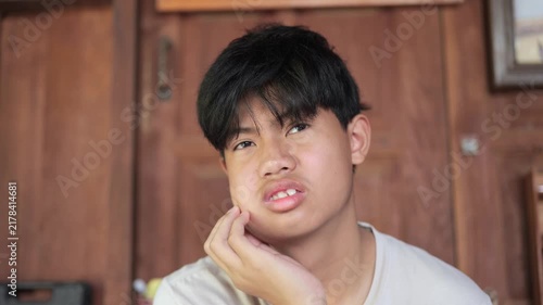 Close-up of a teenage boy grimacing in pain, touching his swollen cheek after wisdom tooth extraction surgery, expressing discomfort from dental pain.