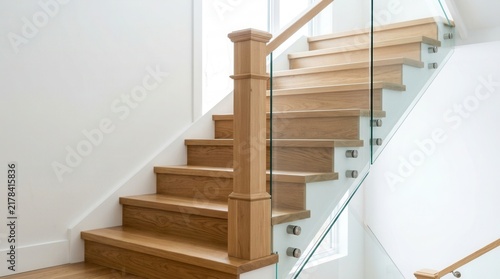 Stairs with wooden treads, transparent glass railing held by steel frames, and a solid newel post