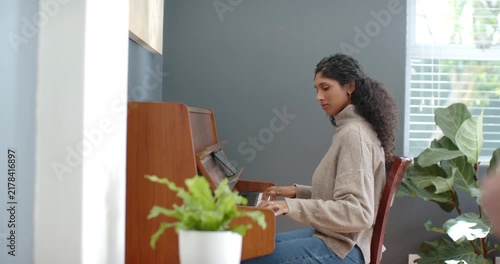 African American woman sitting at upright piano at home, placing hands on keys and practicing piece