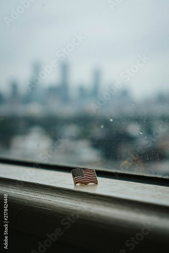 Obraz na płótnie 911, small american flag pin on a windowsill with blurry rainy city skyline view