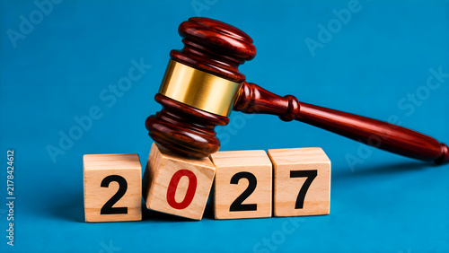 Law gavel striking 2027 wood blocks, judicial concept, legal year prediction, wooden cubes with painted numbers, justice symbol, corporate blue background, courtroom accessories
