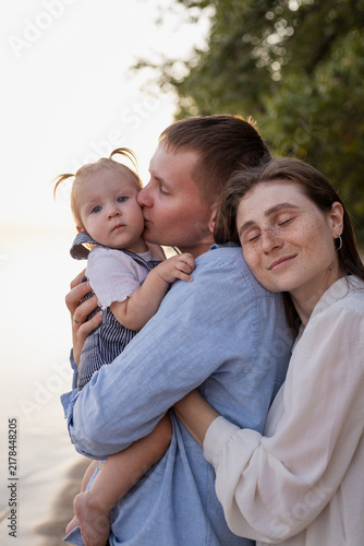Loving parents embrace their baby daughter on a serene beach at sunset