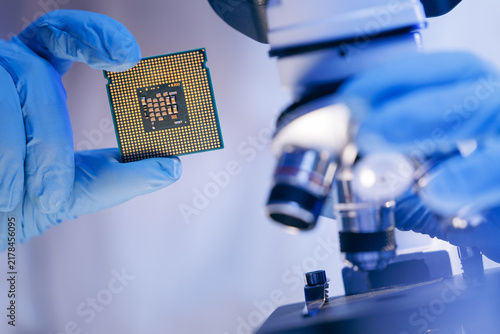 Obraz na plátně Gloved hands holding microprocessor near microscope in laboratory, artificial in