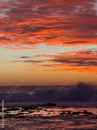 Wall Mural Fiery red and orange clouds sweep across the evening sky above a distant horizon, creating a vivid atmospheric landscape perfect for travel, nature and dramatic background designs
