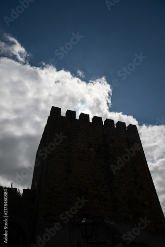 Foto A view of the silhouette of the Óbidos Castle tower against a cloudy sky and sunlight, Portugal