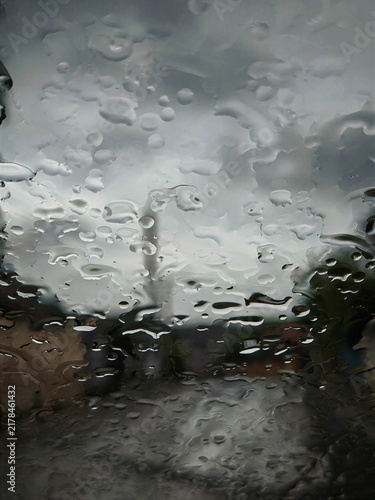 Cuadro en lienzo Detailed raindrops cover a glass window while the landscape beyond fades into soft focus, creating a moody atmospheric image perfect for weather, autumn and conceptual backgrounds