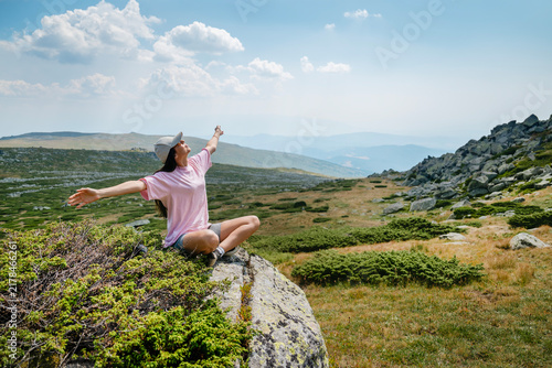 Relaxed woman sitting with open arms high in the summer mountain	