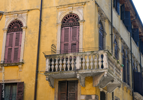 Historic yellow building facade with stone balcony and shuttered windows in Verona, Italy