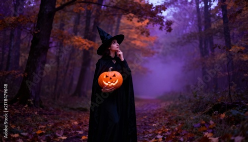 Witch holding glowing jack-o'-lantern in misty autumn forest on Halloween night