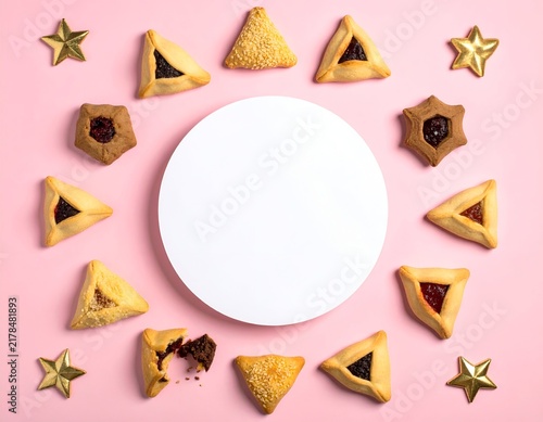 Festive flat lay of Purim hamantaschen cookies, stars, & blank circle on a pink background