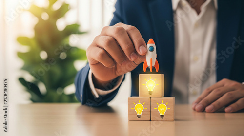 Business startup concept with rocket toy, businessman launching new project on wooden cubes, creative idea and innovation strategy