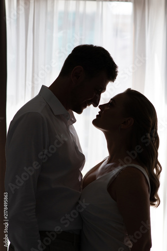 Romantic silhouette portrait of a bride and groom sharing an intimate moment by a window. Soft natural light, elegant wedding atmosphere, love, connection, and timeless emotion.