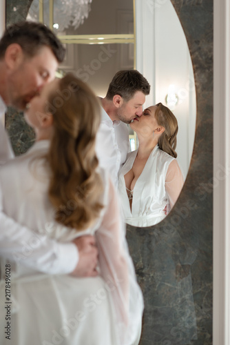 Happy wedding couple embracing and smiling at their reflection in a mirror. Elegant indoor portrait capturing love, connection, and joyful newlywed moments.