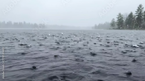 Rain falling on the surface of a lake with misty forest trees in the background with droplets hitting surface video captures rain lake during cloudy day trees distance