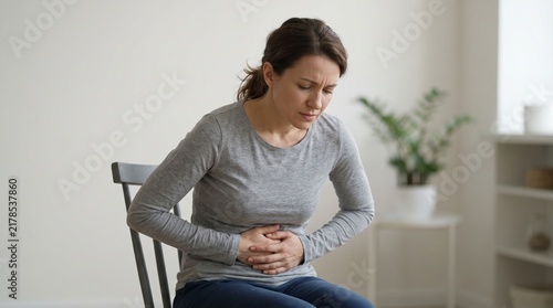 Woman sitting on chair suffering from stomach pain