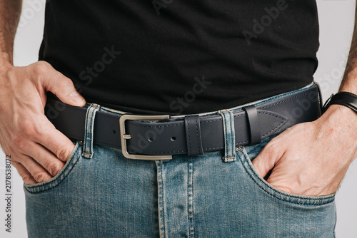 Close-up of a man wearing a dark blue smooth leather belt with a classic metal buckle on black trousers