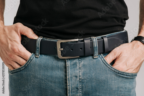 Close-up of a man wearing a dark blue smooth leather belt with a classic metal buckle on blue jeans