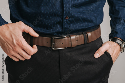 Close-up of a man wearing a brown perforated leather belt with a classic metal buckle on black trousers