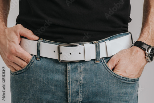 Close-up of a man wearing a white smooth leather belt with a classic metal buckle on blue jeans